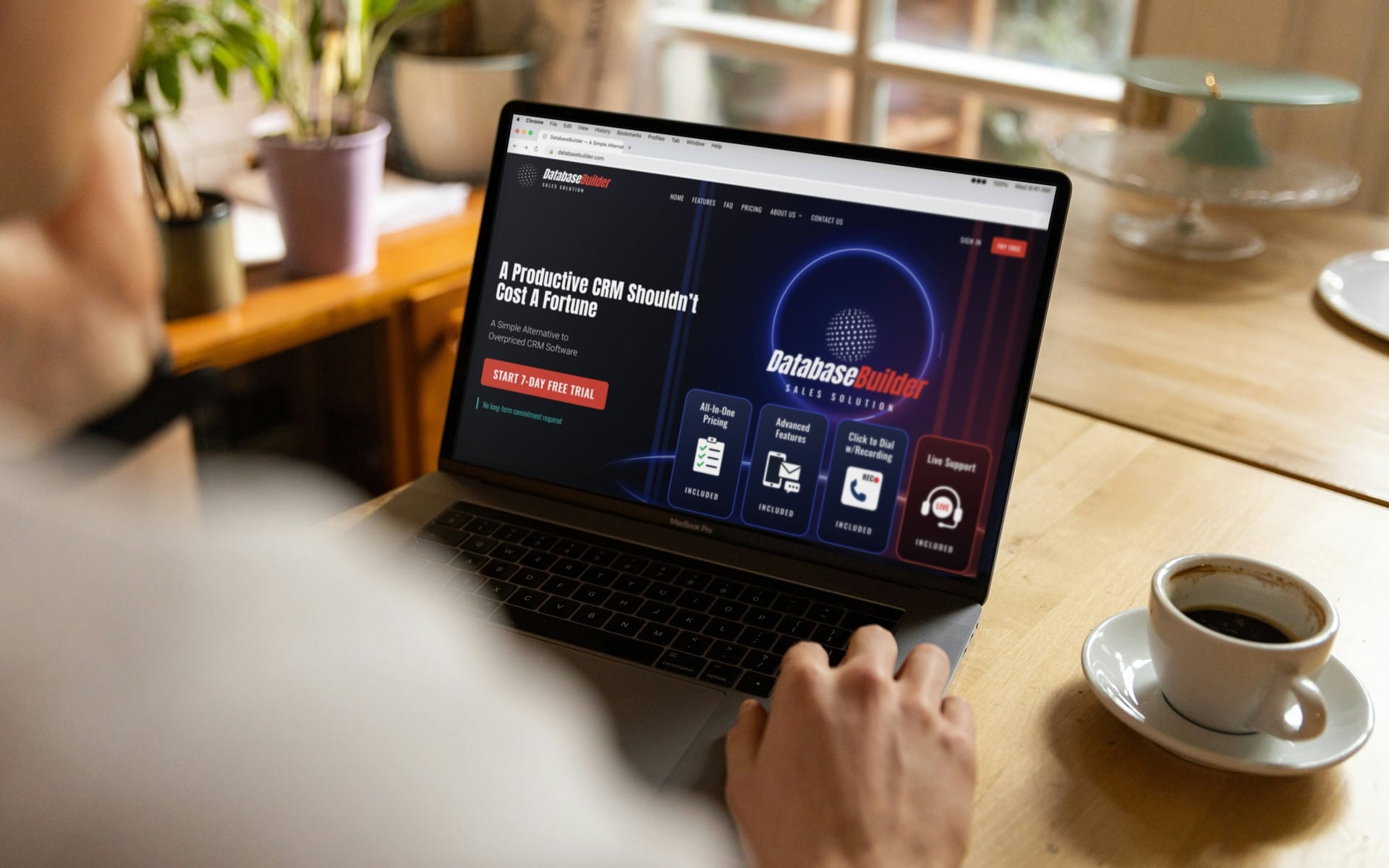 Laptop on a wooden desk showing the DatabaseBuilder sales CRM website, next to a cup of coffee